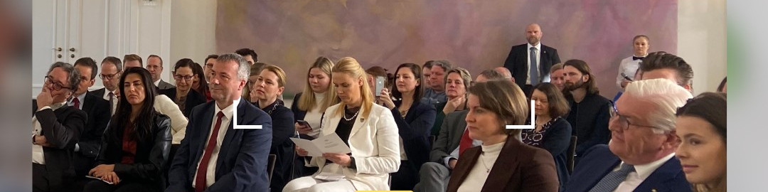 KI generiert: Das Bild zeigt eine Gruppe von Personen, die in einem Raum mit klassischer, eleganter Einrichtung sitzen und einer Veranstaltung oder Präsentation zu folgen scheinen. Der Hauptinhalt des Bildes ist eine formelle Zusammenkunft oder ein Meeting.