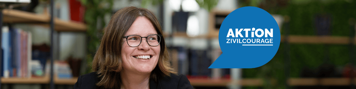 KI generiert: Das Bild zeigt eine lächelnde Frau mit Brille, die vor einem Bücherregal sitzt. Im Vordergrund ist ein blaues Sprechblasen-Symbol mit der Aufschrift "AKTION ZIVILCOURAGE" zu sehen.