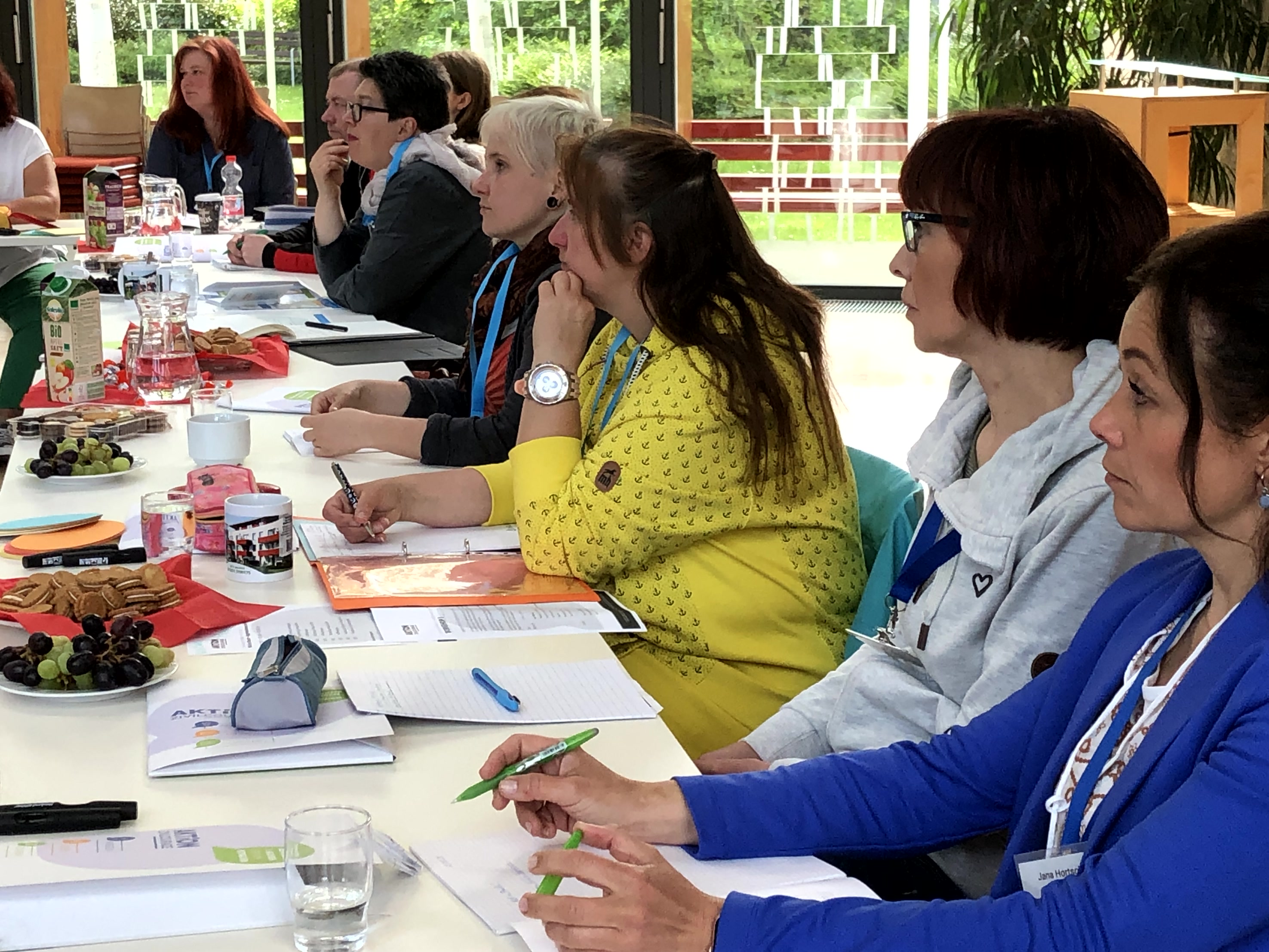 KI generiert: Das Bild zeigt eine Gruppe von Personen, die an einem langen Tisch sitzen und sich auf Notizen oder Unterlagen konzentrieren. Der Hauptinhalt des Bildes ist eine Arbeits- oder Seminar-Situation, in der die Teilnehmerinnen und Teilnehmer aufmerksam zuhören oder arbeiten.