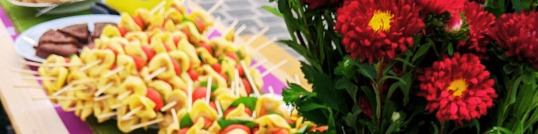 KI generiert: Das Bild zeigt eine Auswahl an bunten, gegrillten Gemüsespießen auf einem Teller sowie eine Vase mit roten und gelben Blumen. Der Hauptinhalt des Bildes sind die farbenfrohen Speisen und die Blumenarrangements.