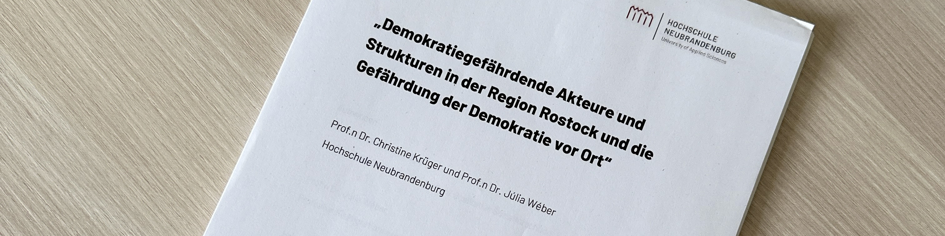 KI generiert: Das Bild zeigt die Titelseite eines Dokuments mit dem Titel "Demokratiegefährdende Akteure und Strukturen in der Region Rostock und die Gefährdung der Demokratie vor Ort". Die Autoren sind Prof.in Dr. Christine Krüger und Prof.in Dr. Julia Weber von der Hochschule Neubrandenburg.