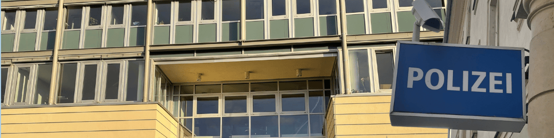 KI generiert: Das Bild zeigt ein mehrstöckiges Gebäude mit vielen Fenstern und einem blauen Schild mit der Aufschrift "POLIZEI" im Vordergrund. Der Hauptinhalt des Bildes ist ein Polizeigebäude.