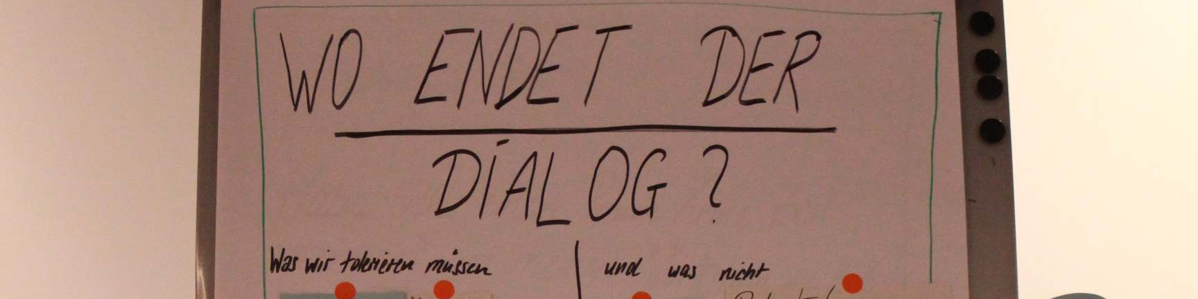 KI generiert: Das Bild zeigt eine Tafel oder ein Whiteboard mit der handschriftlichen Frage "WO ENDET DER DIALOG?" in großer Schrift. Darunter stehen weitere handschriftliche Notizen in kleinerer Schrift, die jedoch nicht vollständig lesbar sind.