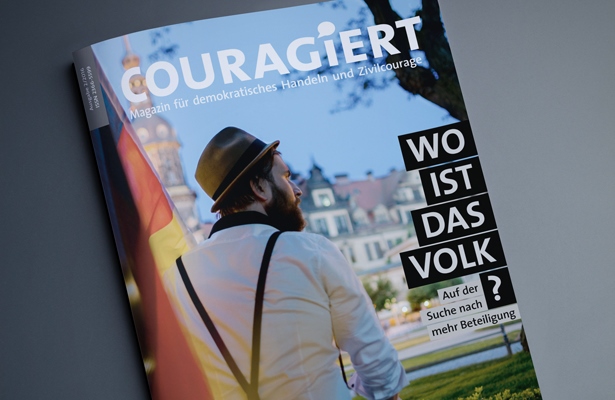 KI generiert: Das Bild zeigt das Cover einer Ausgabe des Magazins "COURAGIERT" mit dem Titel "WO IST DAS VOLK? Auf der Suche nach mehr Beteiligung". Im Vordergrund ist ein Mann mit Hut und Rucksack zu sehen, der vor einer Stadtkulisse steht.