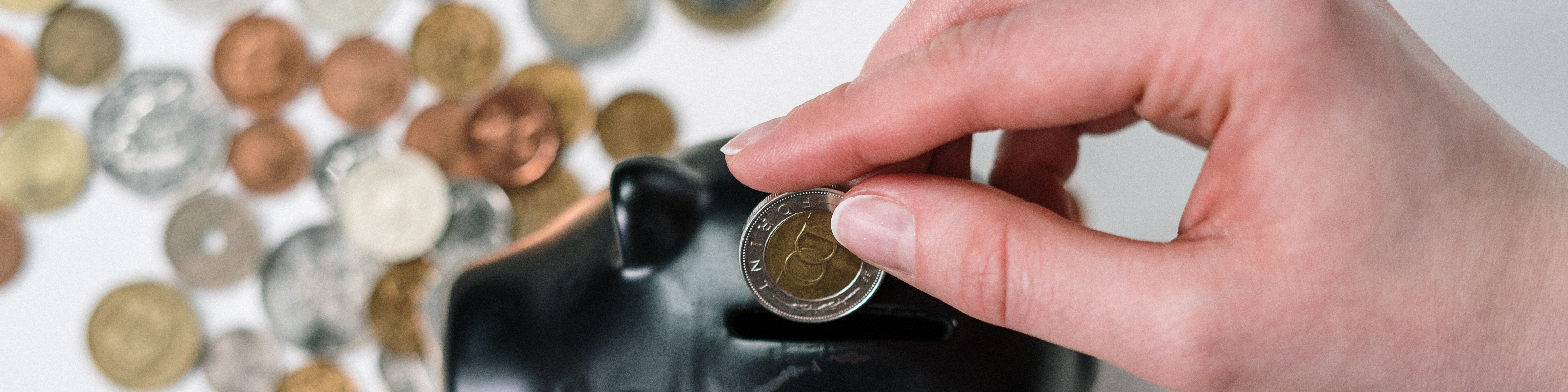 KI generiert: Eine Hand steckt eine Münze in ein schwarzes Sparschwein, während verschiedene Münzen im Hintergrund verstreut sind. Der Hauptinhalt des Bildes ist das Konzept des Sparens oder der finanziellen Vorsorge.