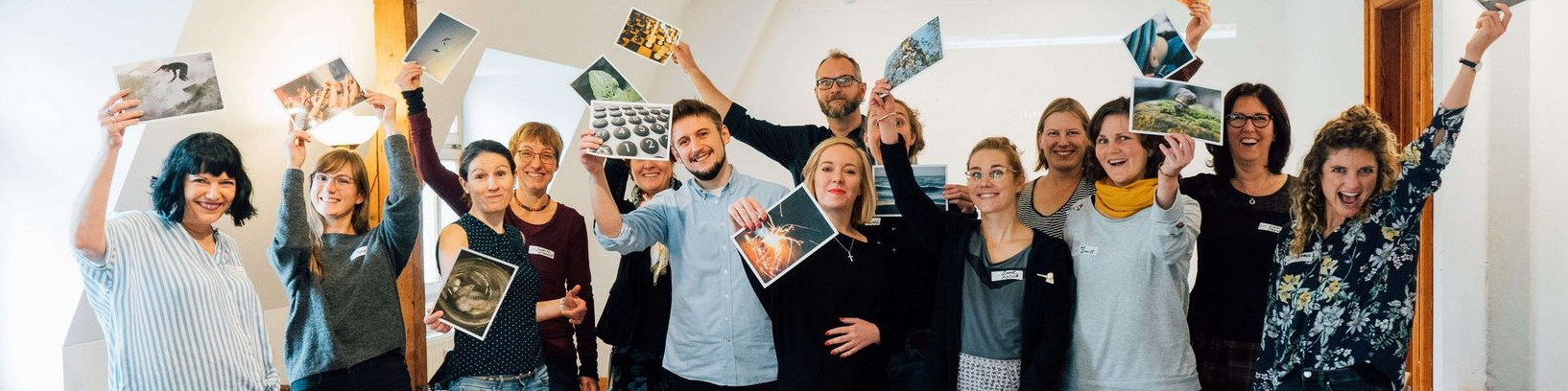 KI generiert: Das Bild zeigt eine Gruppe von Menschen, die gemeinsam in einem Raum stehen und freudig Fotos in die Höhe halten. Der Hauptinhalt des Bildes ist eine fröhliche und gesellige Atmosphäre, in der die Gruppe ihre Fotos teilt und präsentiert.