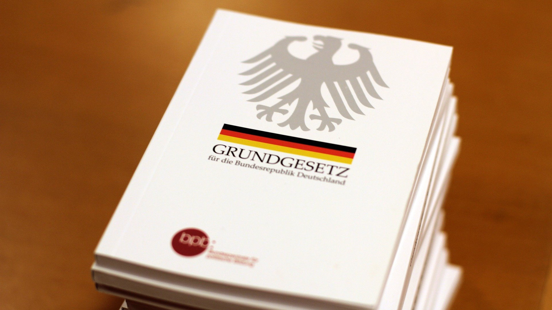 KI generiert: Das Bild zeigt mehrere Stapel des Grundgesetzes für die Bundesrepublik Deutschland, erkennbar an der Aufschrift und dem Bundesadler auf dem weißen Einband. Der Hauptinhalt des Bildes sind also die Exemplare der deutschen Verfassung.