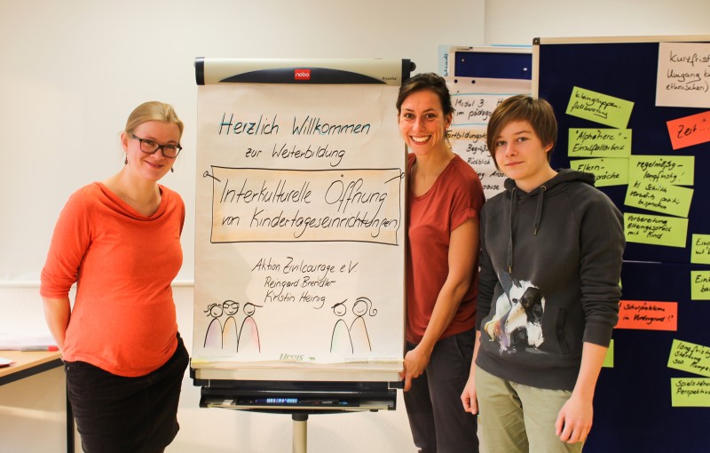 KI generiert: Das Bild zeigt drei Personen, die vor einem Flipchart stehen, auf dem "Herzlich Willkommen zur Weiterbildung - Interkulturelle Öffnung von Kindertageseinrichtungen" geschrieben steht. Der Hauptinhalt des Bildes ist eine Weiterbildungsveranstaltung zum Thema interkulturelle Öffnung in Kindertageseinrichtungen.