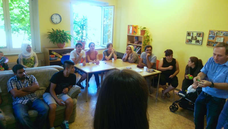 KI generiert: Das Bild zeigt eine Gruppe von Menschen, die in einem hellen Raum mit gelben Wänden sitzen und sich unterhalten. Der Hauptinhalt des Bildes ist eine gesellige Zusammenkunft oder ein Treffen, bei dem die Teilnehmer in einer entspannten Atmosphäre interagieren.