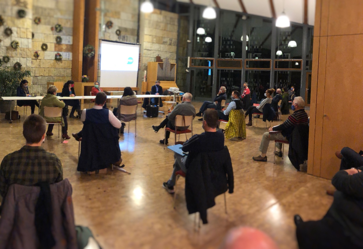 KI generiert: Das Bild zeigt eine Gruppe von Personen, die in einem großen, rustikalen Raum mit Holzboden und Steinwänden an einem Seminar oder einer Präsentation teilnehmen. Der Hauptinhalt ist eine Bildungsveranstaltung, bei der eine Person vorne präsentiert und die anderen zuhören.