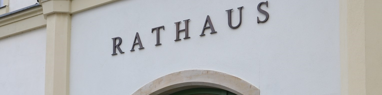 KI generiert: Das Bild zeigt die Fassade eines Gebäudes mit dem Namen "RATHAUS" in großen, dunklen Buchstaben an der Wand. Der Hauptinhalt des Bildes ist die Kennzeichnung des Gebäudes als Rathaus.