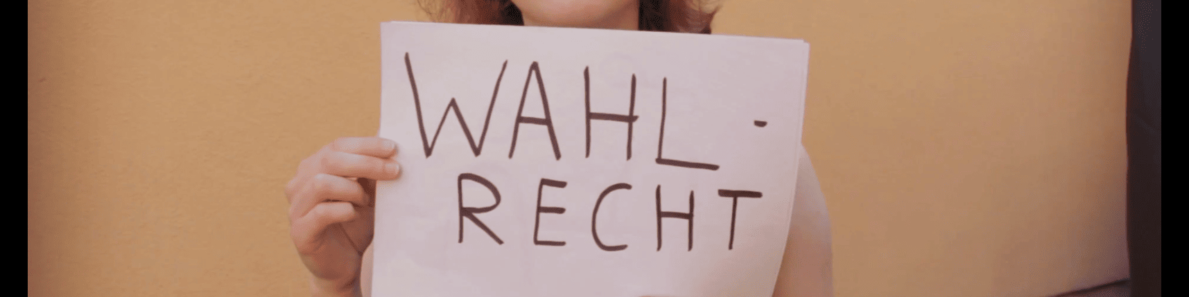 KI generiert: Das Bild zeigt eine Person, die ein weißes Blatt Papier mit der Aufschrift "WAHL-RECHT" in die Kamera hält. Der Hauptinhalt des Bildes ist die Forderung nach Wahlrecht.