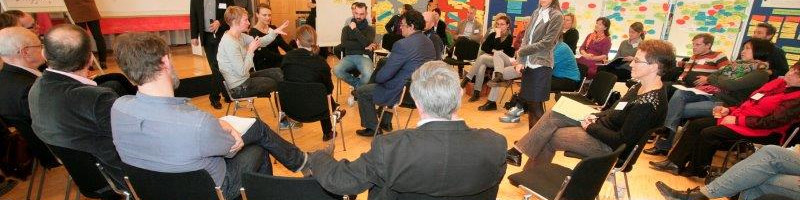 KI generiert: Das Bild zeigt eine Gruppe von Personen, die in einem Kreis sitzen und sich in einer Besprechung oder einem Workshop befinden. Der Hauptinhalt des Bildes ist eine interaktive Diskussion oder ein Meeting in einem informellen Rahmen.