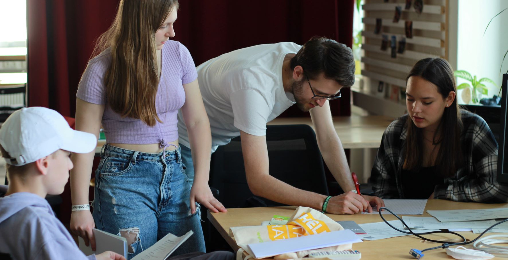 KI generiert: Das Bild zeigt eine Gruppe von vier Personen, die an einem Tisch zusammenarbeiten, wobei sie sich auf verschiedene Unterlagen und ein Laptop konzentrieren. Der Hauptinhalt des Bildes ist eine kollaborative Arbeits- oder Lernsituation.