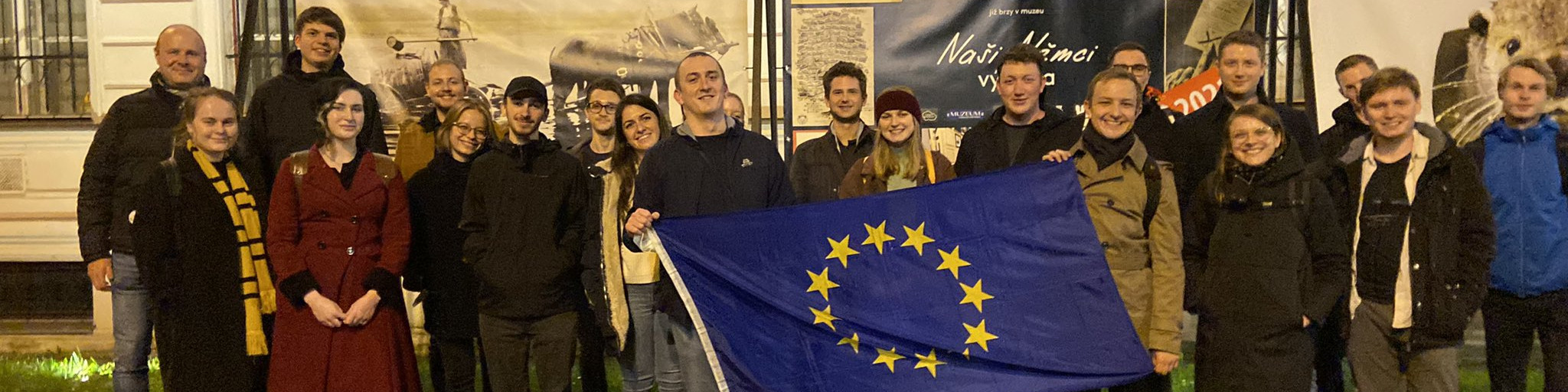 KI generiert: Das Bild zeigt eine Gruppe von Menschen, die gemeinsam vor einem Gebäude stehen und die Flagge der Europäischen Union halten. Der Hauptinhalt des Bildes ist die Darstellung einer Gruppe, die möglicherweise an einer europäischen Veranstaltung oder einem Treffen teilnimmt.