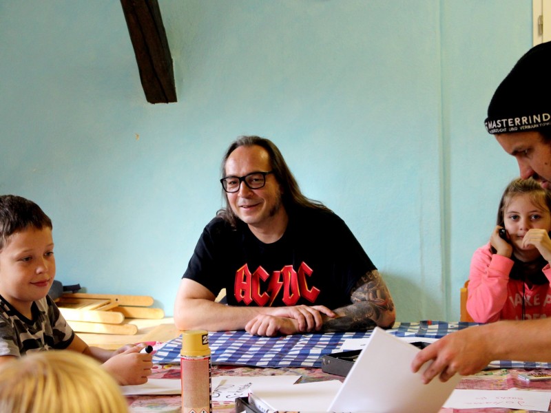 KI generiert: Das Bild zeigt eine Gruppe von Personen, darunter Kinder und Erwachsene, die an einem Tisch sitzen und sich auf ein Spiel oder eine Aktivität konzentrieren. Der Hauptinhalt des Bildes ist eine gesellige Runde, die gemeinsam Zeit verbringt und möglicherweise ein Brettspiel spielt.