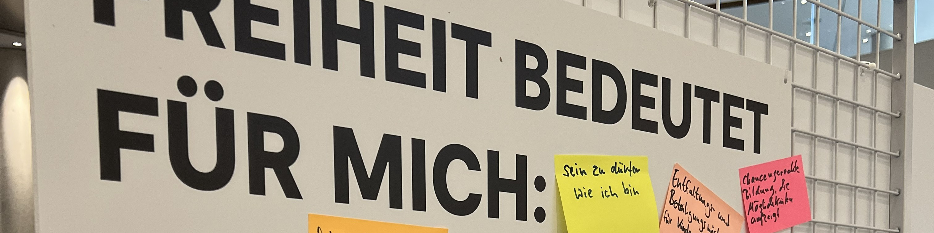 KI generiert: Das Bild zeigt einen Ausschnitt eines Plakats mit dem Text "FREIHEIT BEDEUTET FÜR MICH:" und mehreren bunten Klebezetteln, auf denen individuelle Antworten geschrieben sind. Der Hauptinhalt des Bildes ist die Darstellung verschiedener persönlicher Definitionen von Freiheit.