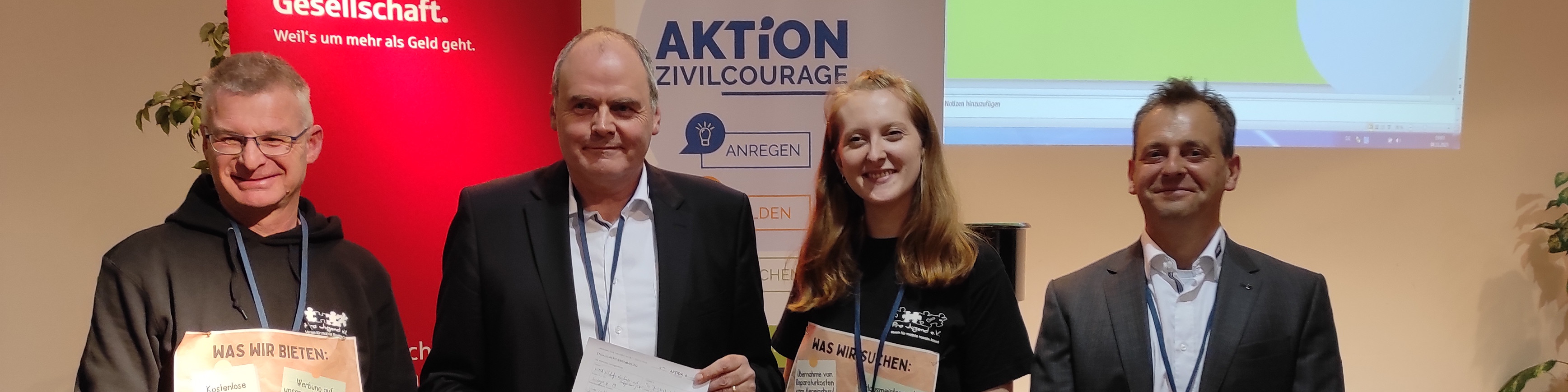 KI generiert: Das Bild zeigt vier Personen, die vor einem Banner mit der Aufschrift "AKTION ZIVILCOURAGE" stehen und Dokumente in den Händen halten. Es scheint sich um eine Veranstaltung oder Auszeichnung im Zusammenhang mit Zivilcourage zu handeln.