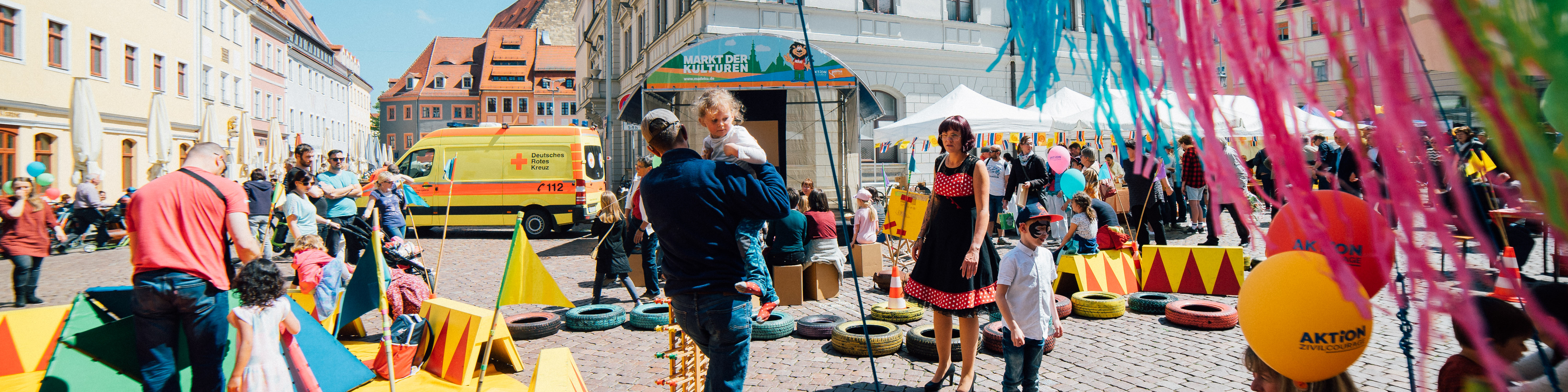 KI generiert: Das Bild zeigt eine belebte Straßenveranstaltung mit vielen Menschen, bunten Dekorationen und Spielstationen für Kinder. Im Mittelpunkt stehen Familien, die gemeinsam verschiedene Aktivitäten genießen.