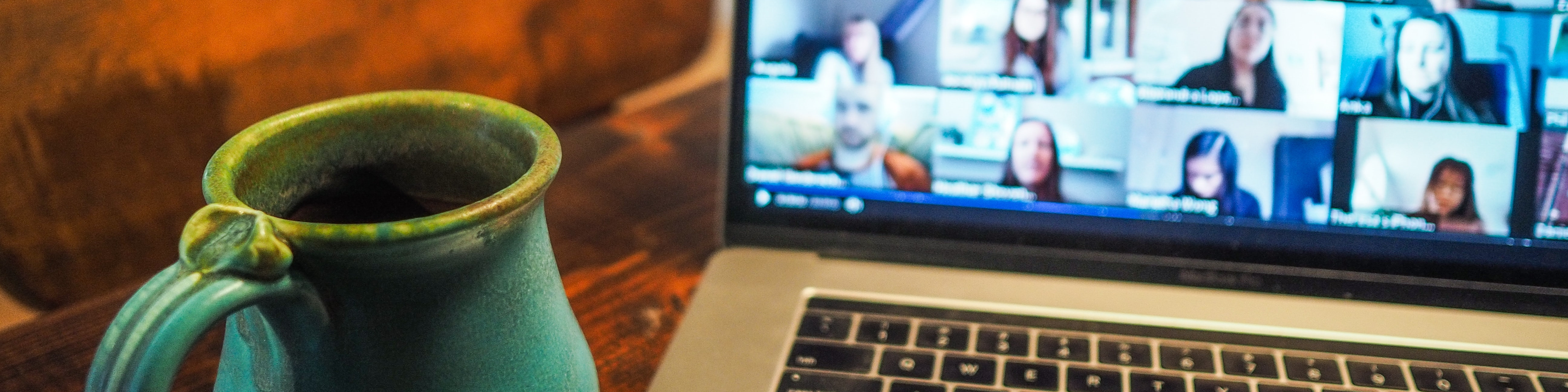 KI generiert: Das Bild zeigt einen Laptop mit einer laufenden Videokonferenz auf dem Bildschirm, bei der mehrere Personen in kleinen Fenstern zu sehen sind. Im Vordergrund steht eine grüne Keramik-Tasse.