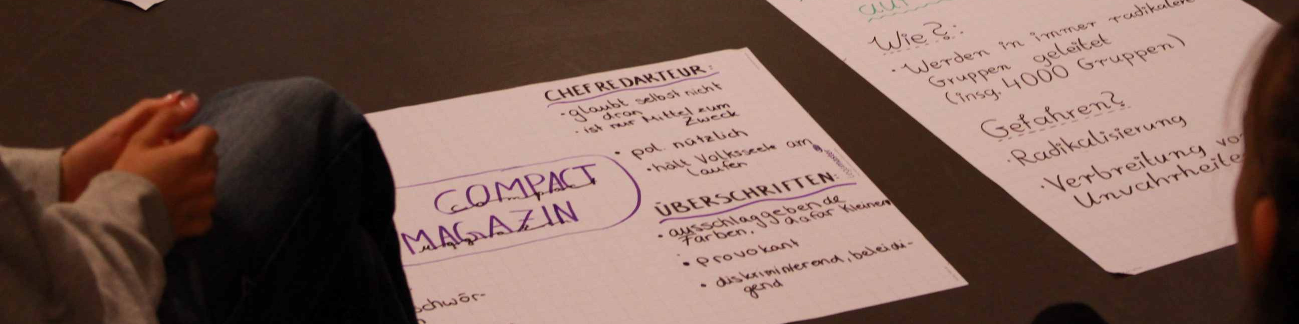 KI generiert: Das Bild zeigt eine Person, die an einem Tisch sitzt und auf einem Blatt Papier Notizen macht. Der Hauptinhalt des Bildes sind die handschriftlichen Notizen auf dem Papier, die sich auf das Thema "Compact Magazin" beziehen.