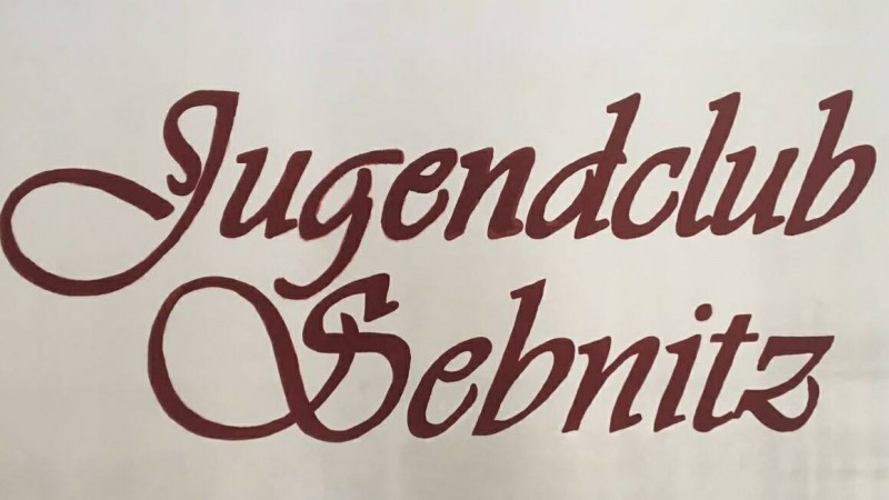 KI generiert: Das Bild zeigt das Logo des Jugendclubs Sebnitz, wobei der Text "Jugendclub Sebnitz" in einer verschnörkelten, maroonfarbenen Schrift auf einem hellen Hintergrund dargestellt ist. Der Hauptinhalt des Bildes ist der Name des Jugendclubs.