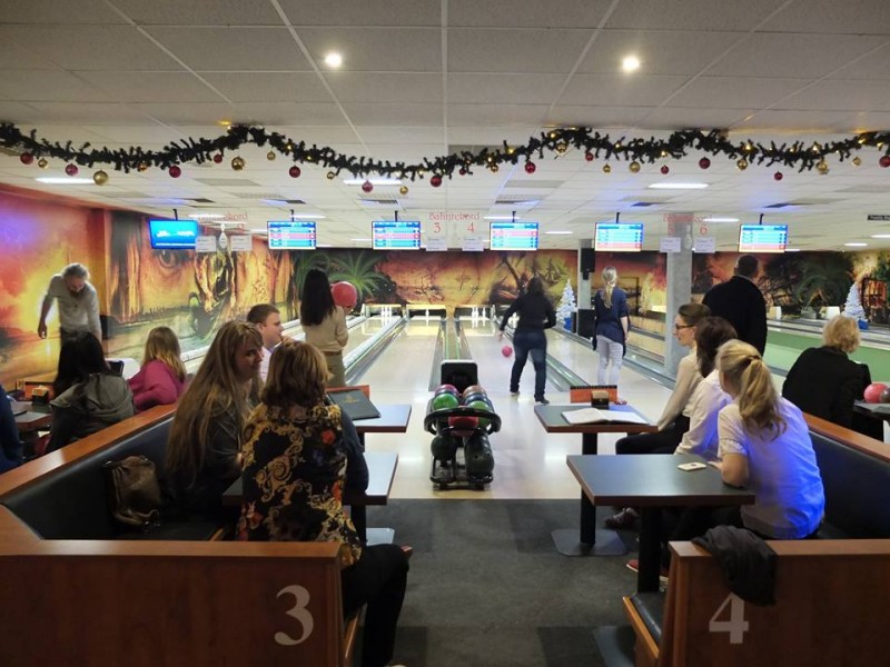 KI generiert: Das Bild zeigt eine Bowlingbahn mit mehreren Personen, die entweder bowlen oder zuschauen. Die Bahn ist festlich mit Girlanden und Lichtern geschmückt, was auf eine Feier oder besondere Veranstaltung hindeutet.