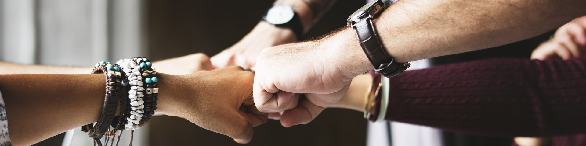 KI generiert: Das Bild zeigt mehrere Hände, die sich in der Mitte zu einem festen Handschlag vereinen, was Teamwork und Zusammenhalt symbolisiert. Die Personen tragen verschiedene Armbänder und Uhren, was auf Individualität hinweist.