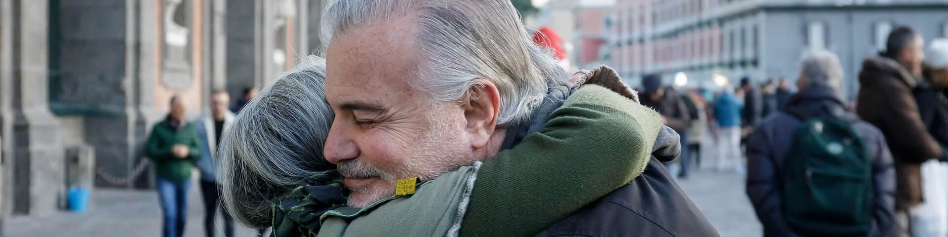 KI generiert: Das Bild zeigt eine herzliche Umarmung zwischen zwei älteren Personen auf einer belebten Straße. Der Hauptinhalt ist die emotionale Geste der Zuneigung und Verbundenheit zwischen den beiden Menschen.