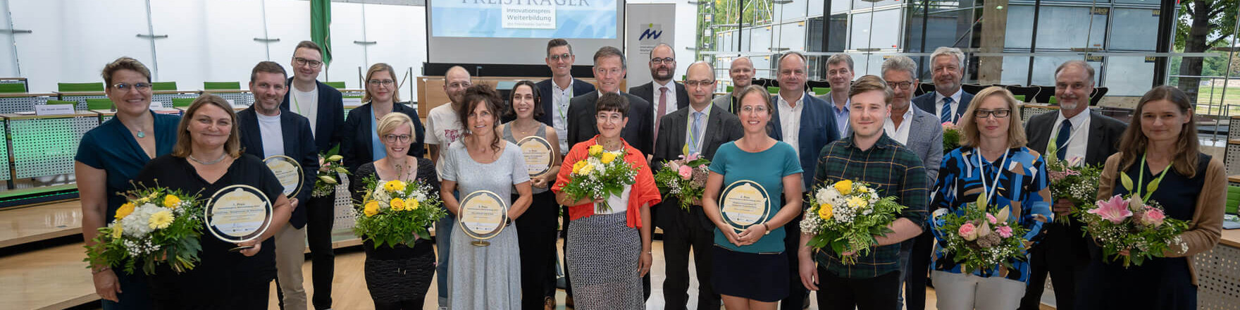 KI generiert: Das Bild zeigt eine Gruppe von Menschen, die in einem hellen Raum stehen und Blumensträuße sowie Urkunden oder Preise in den Händen halten. Es scheint sich um eine feierliche Veranstaltung oder eine Preisverleihung zu handeln.