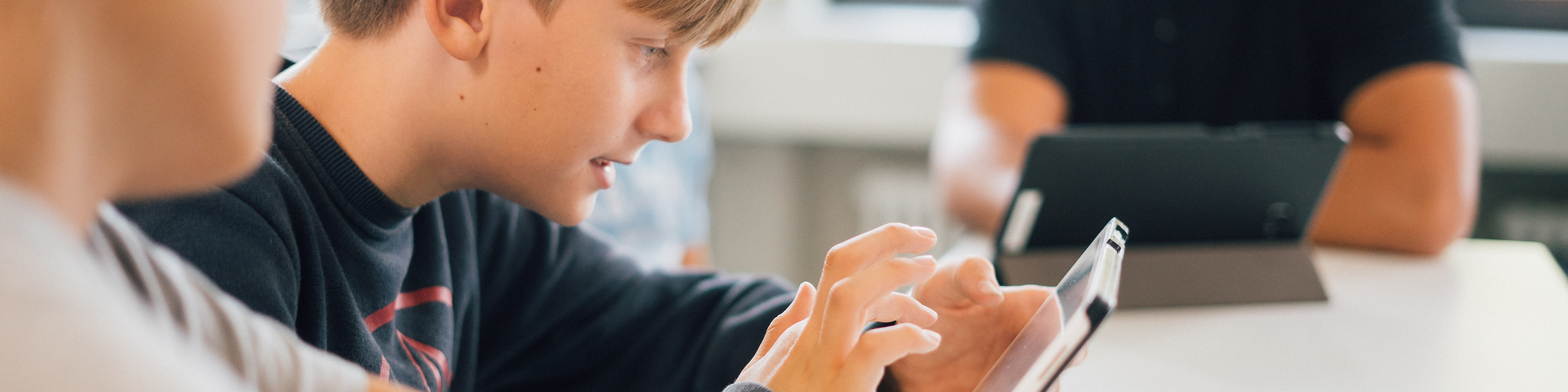 KI generiert: Das Bild zeigt eine Gruppe von Personen, die an einem Tisch sitzen und auf Tablets oder Laptops arbeiten. Der Hauptinhalt des Bildes ist eine Lernsituation oder ein Workshop, bei dem digitale Geräte genutzt werden.