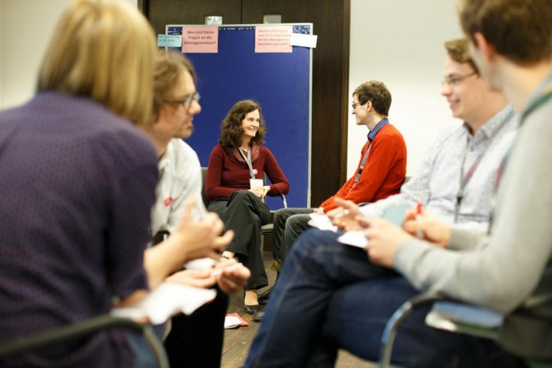 KI generiert: Das Bild zeigt eine Gruppe von Personen, die in einem Kreis sitzen und sich in einer Diskussion oder einem Meeting befinden. Der Hauptinhalt des Bildes ist eine interaktive Gruppendiskussion oder ein Workshop.