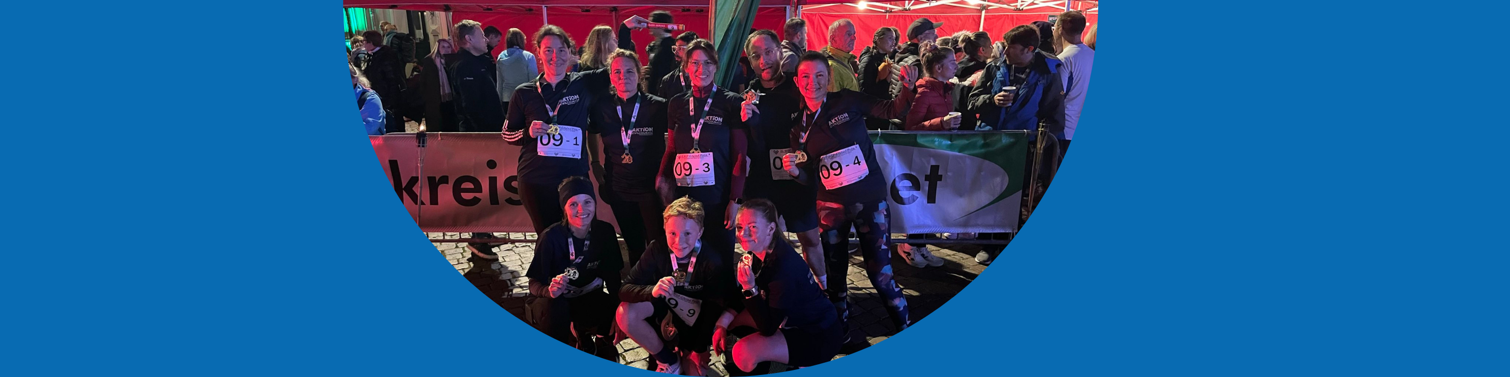 KI generiert: Das Bild zeigt eine Gruppe von Personen, die an einem Event teilnehmen, möglicherweise einem Sportwettbewerb oder einer Gemeinschaftsveranstaltung. Die Teilnehmer tragen Nummernschilder und Medaillen, was darauf hindeutet, dass sie eine Aktivität abgeschlossen haben.