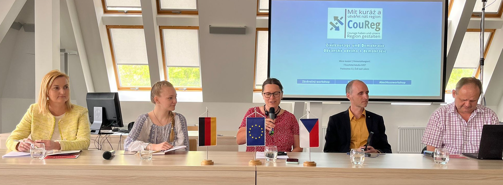KI generiert: Das Bild zeigt eine Gruppe von fünf Personen, die an einem langen Tisch sitzen und an einer Besprechung oder Konferenz teilnehmen. Im Hintergrund ist eine Projektionsleinwand mit dem Logo und dem Namen "CouReg" sowie Text in deutscher Sprache zu sehen, was auf eine formelle Veranstaltung hinweist.