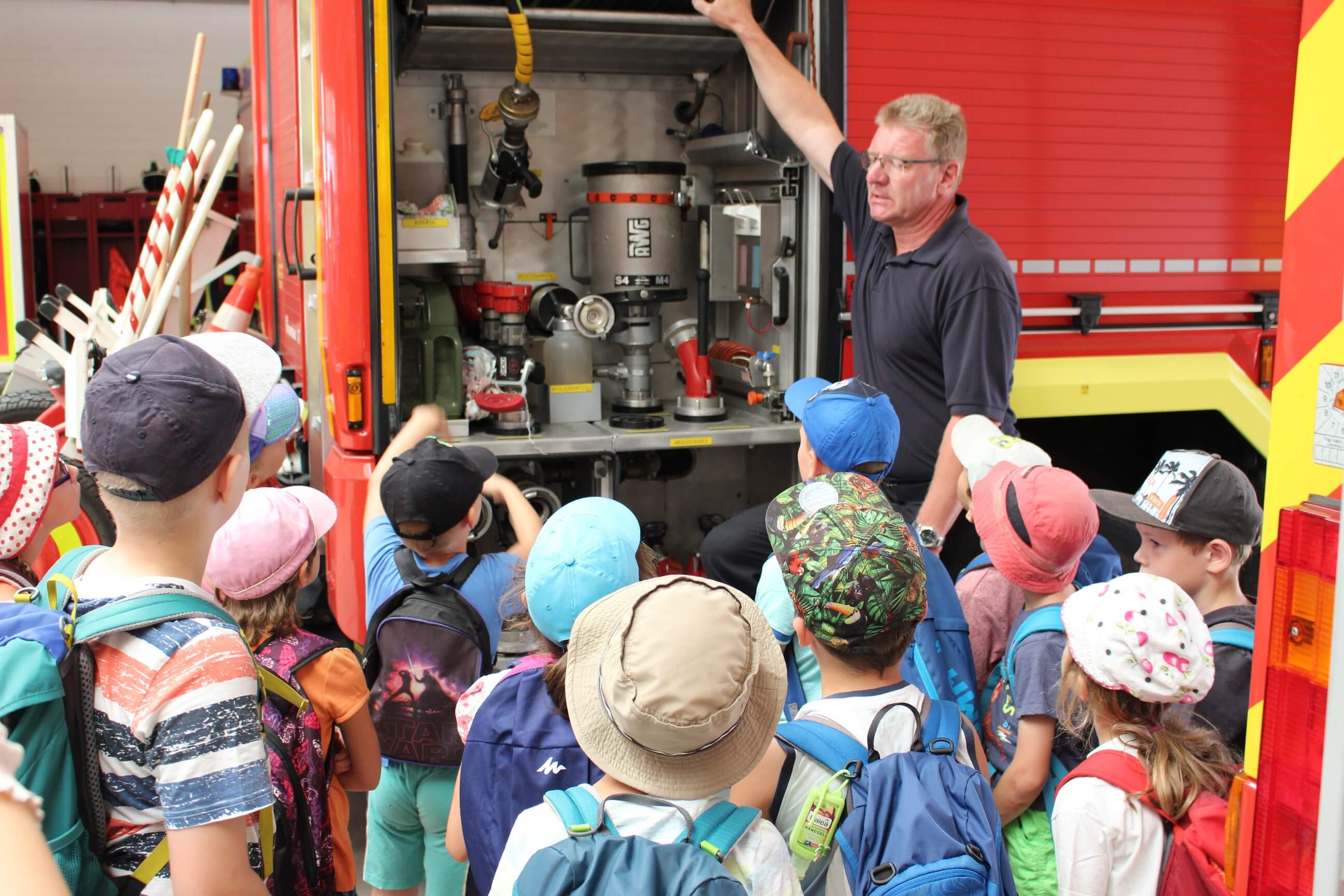 KI generiert: Das Bild zeigt eine Gruppe von Kindern, die sich um einen Mann versammelt haben, der ihnen die Ausrüstung eines Feuerwehrautos erklärt. Der Hauptinhalt des Bildes ist eine Bildungsveranstaltung, bei der Kinder über die Funktionsweise von Feuerwehrautos informiert werden.