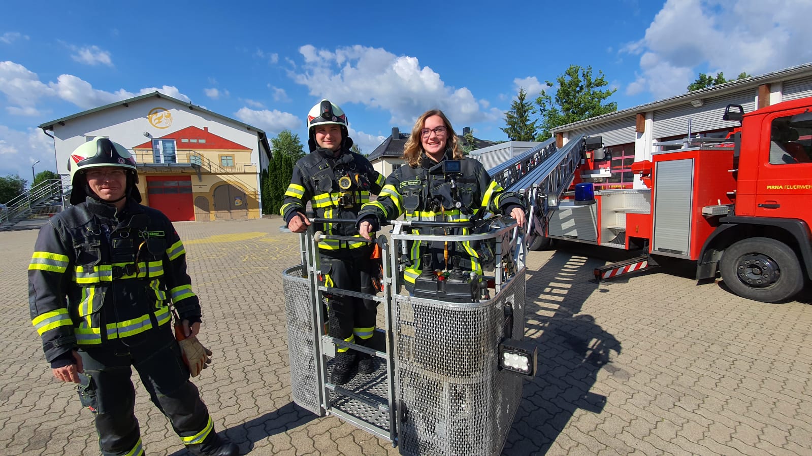 KI generiert: Das Bild zeigt drei Feuerwehrleute in voller Schutzausrüstung, die vor einem Feuerwehrfahrzeug und einer Feuerwache posieren. Im Vordergrund steht ein spezielles Rettungsgerät, möglicherweise eine Trage oder ein Transportbehälter.