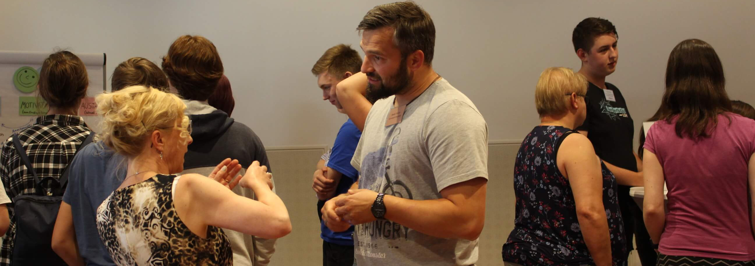 KI generiert: Das Bild zeigt eine Gruppe von Menschen in einem Innenraum, die sich in kleinen Gruppen unterhalten. Der Hauptinhalt des Bildes ist eine soziale Interaktion oder ein Treffen, bei dem die Teilnehmer miteinander sprechen und sich austauschen.