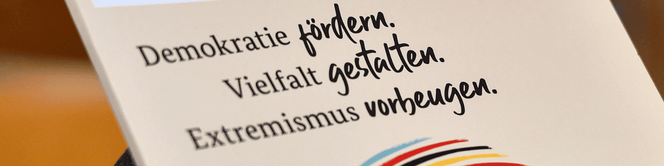KI generiert: Das Bild zeigt einen Ausschnitt eines Dokuments oder einer Broschüre mit dem Text "Demokratie fördern. Vielfalt gestalten. Extremismus vorbeugen." Der Hauptinhalt des Bildes ist die Förderung von Demokratie und Vielfalt sowie die Prävention von Extremismus.