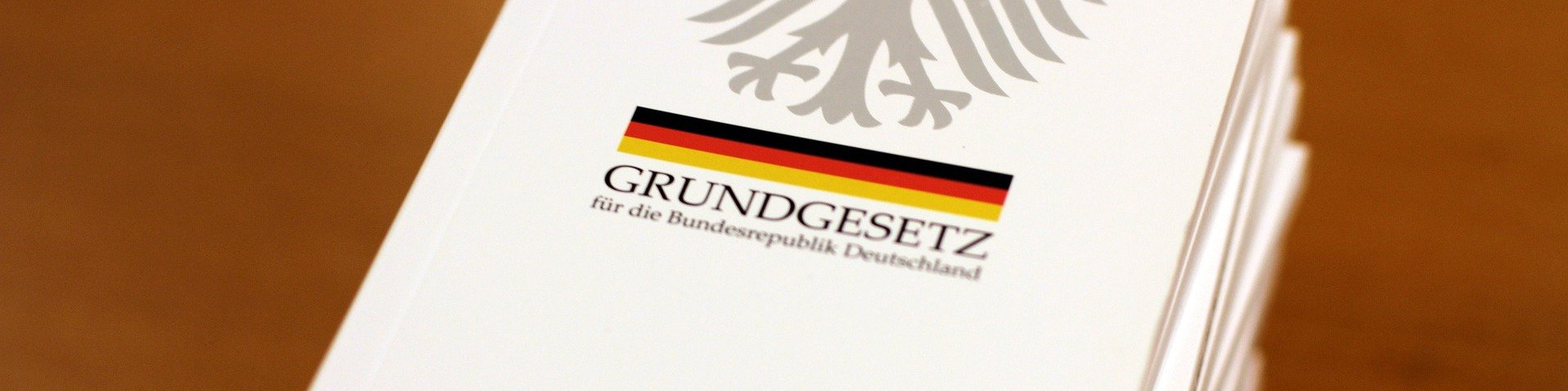 KI generiert: Das Bild zeigt ein Stapel von Dokumenten mit dem Aufdruck "GRUNDGESETZ für die Bundesrepublik Deutschland" und dem Bundesadler. Der Hauptinhalt des Bildes ist das Grundgesetz, die Verfassung der Bundesrepublik Deutschland.