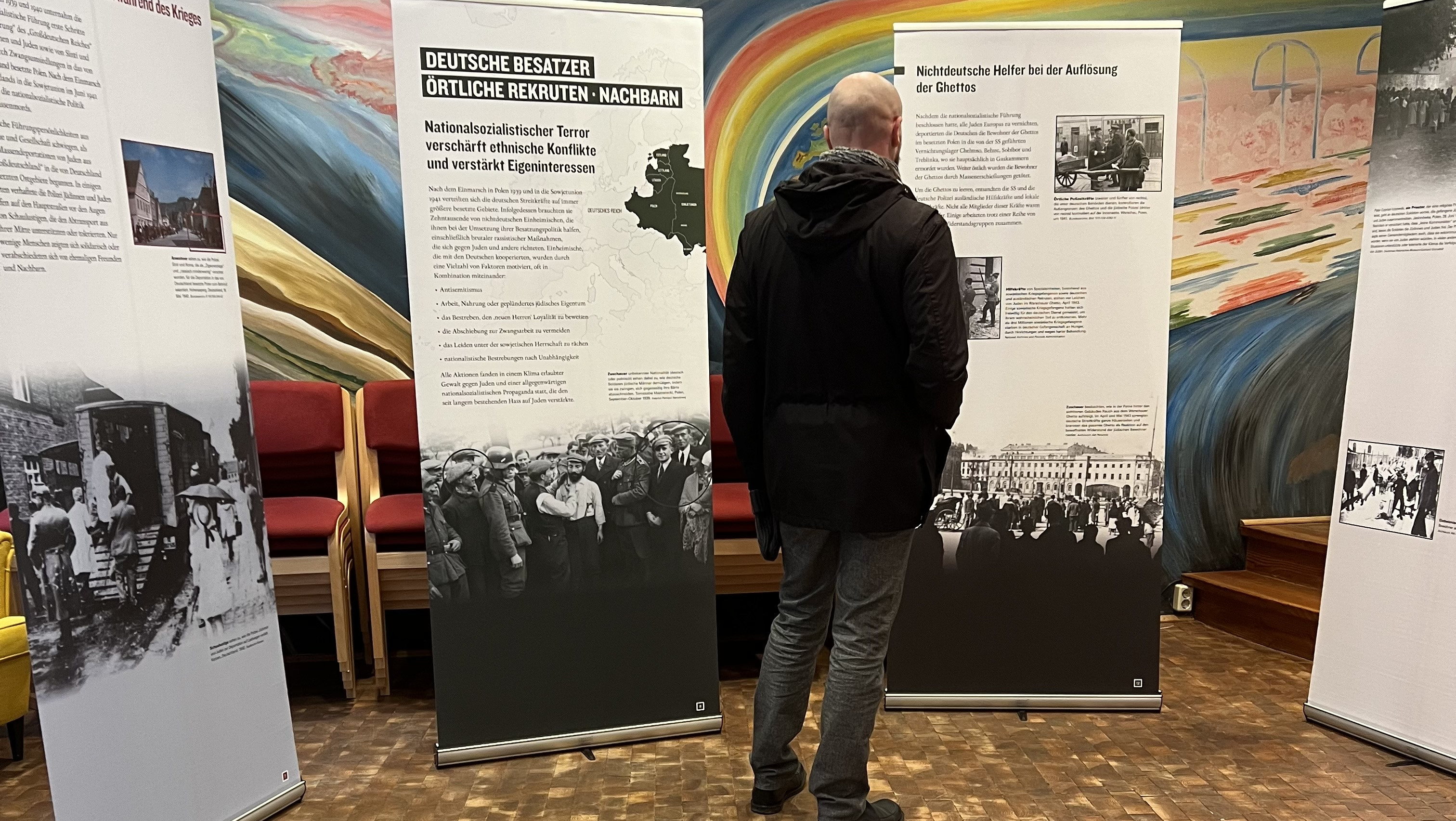 KI generiert: Das Bild zeigt einen Mann, der eine Ausstellung in einem Innenraum besucht und sich Informationsplakate ansieht, die historische Fotos und Texte enthalten. Der Hauptinhalt der Ausstellung scheint sich auf historische Ereignisse, möglicherweise im Zusammenhang mit dem Nationalsozialismus und dem Widerstand, zu beziehen.