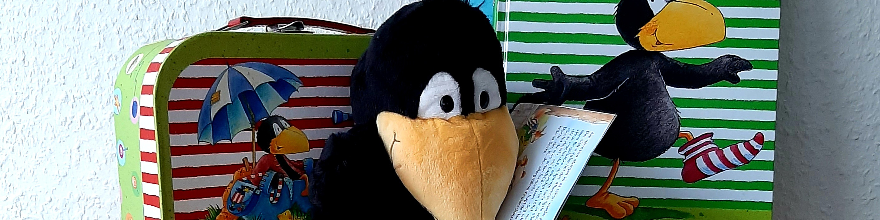 KI generiert: Das Bild zeigt ein Stofftier in Form eines Raben, das ein Buch in den Flügeln hält. Im Hintergrund ist eine Kindertragtasche mit bunten Motiven zu sehen.