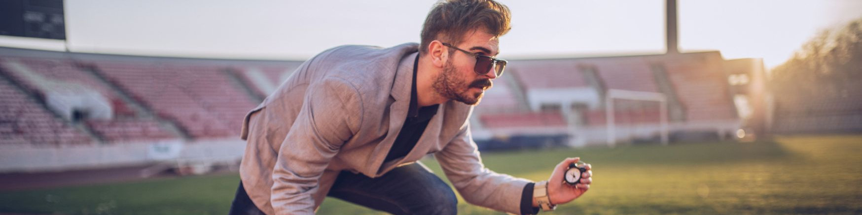 KI generiert: Das Bild zeigt einen Mann in einem Stadion, der sich in einer gebückten Haltung befindet und eine Stoppuhr in der Hand hält. Der Hauptinhalt des Bildes ist die Darstellung eines Sportlers oder Trainers, der möglicherweise eine Zeitmessung während eines Trainings oder Wettbewerbs durchführt.