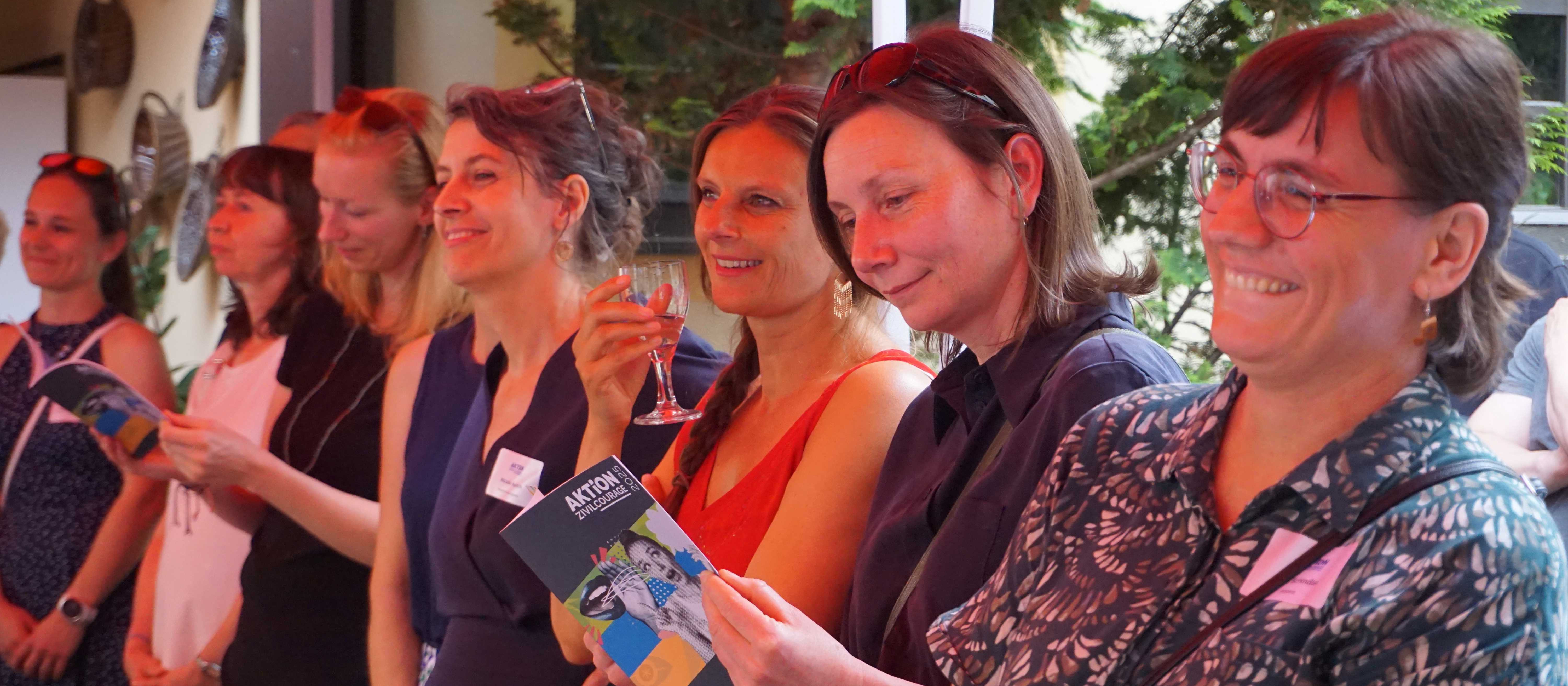 KI generiert: Das Bild zeigt eine Gruppe von Menschen, die sich in einer geselligen Runde befinden, wobei einige Gläser in der Hand halten und sich unterhalten. Der Hauptinhalt des Bildes ist eine gesellige Zusammenkunft oder ein Event, bei dem die Teilnehmer entspannt und fröhlich wirken.