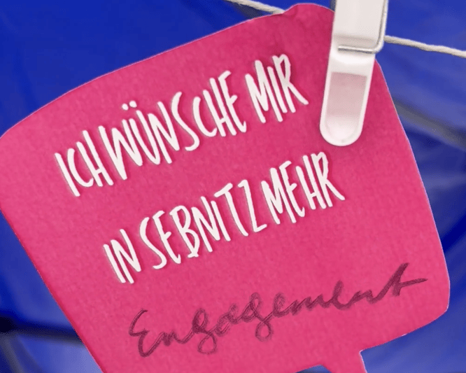 KI generiert: Das Bild zeigt eine Gruppe junger Frauen, die in einer Freiluftveranstaltung eine choreografierte Tanzdarbietung aufführen. Im Hintergrund sitzt ein Publikum, das die Darstellung beobachtet, während im Hintergrund bunte Zelte und ein Gebäude zu sehen sind.