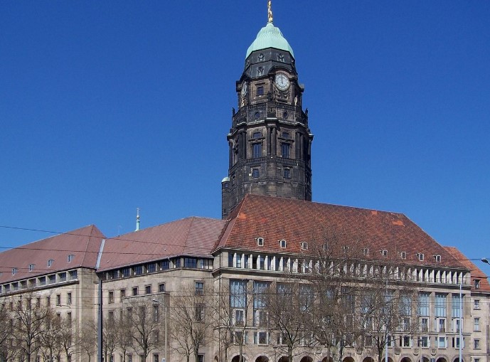KI generiert: Das Bild zeigt ein imposantes historisches Gebäude mit einem markanten Uhrturm und einem grünen Kuppeldach. Der Hauptinhalt des Bildes ist der Turm und das dazugehörige Gebäude, das vermutlich ein Rathaus oder ein anderes bedeutendes öffentliches Gebäude ist.