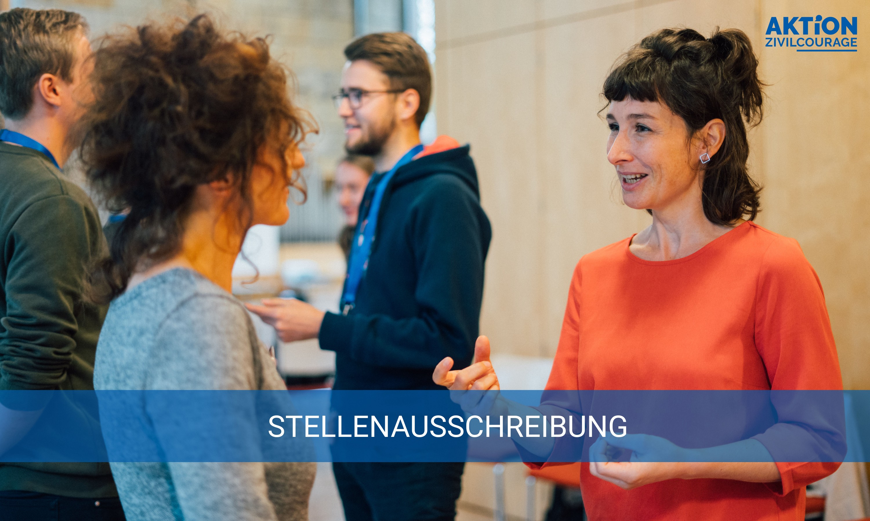 KI generiert: Das Bild zeigt eine Gruppe von Personen, die sich in einer informellen Umgebung unterhalten, wobei eine Frau in einem orangen Pullover im Vordergrund steht und mit einer anderen Person spricht. Der Hauptinhalt des Bildes ist eine Stellenausschreibung, wie durch die Textzeile "STELLENAUSSCHREIBUNG" angezeigt wird.