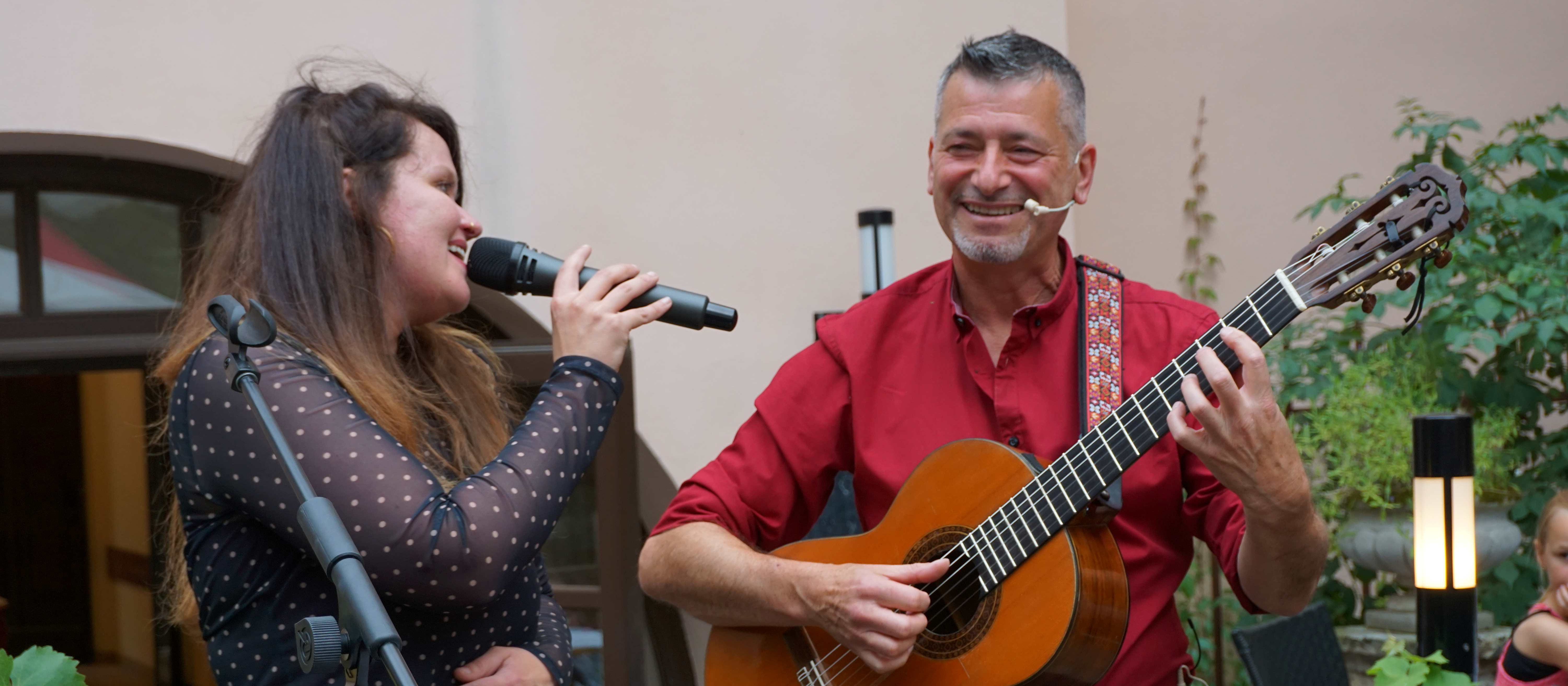 KI generiert: Das Bild zeigt eine Frau und einen Mann, die gemeinsam Musik machen. Die Frau singt in ein Mikrofon, während der Mann eine Gitarre spielt.
