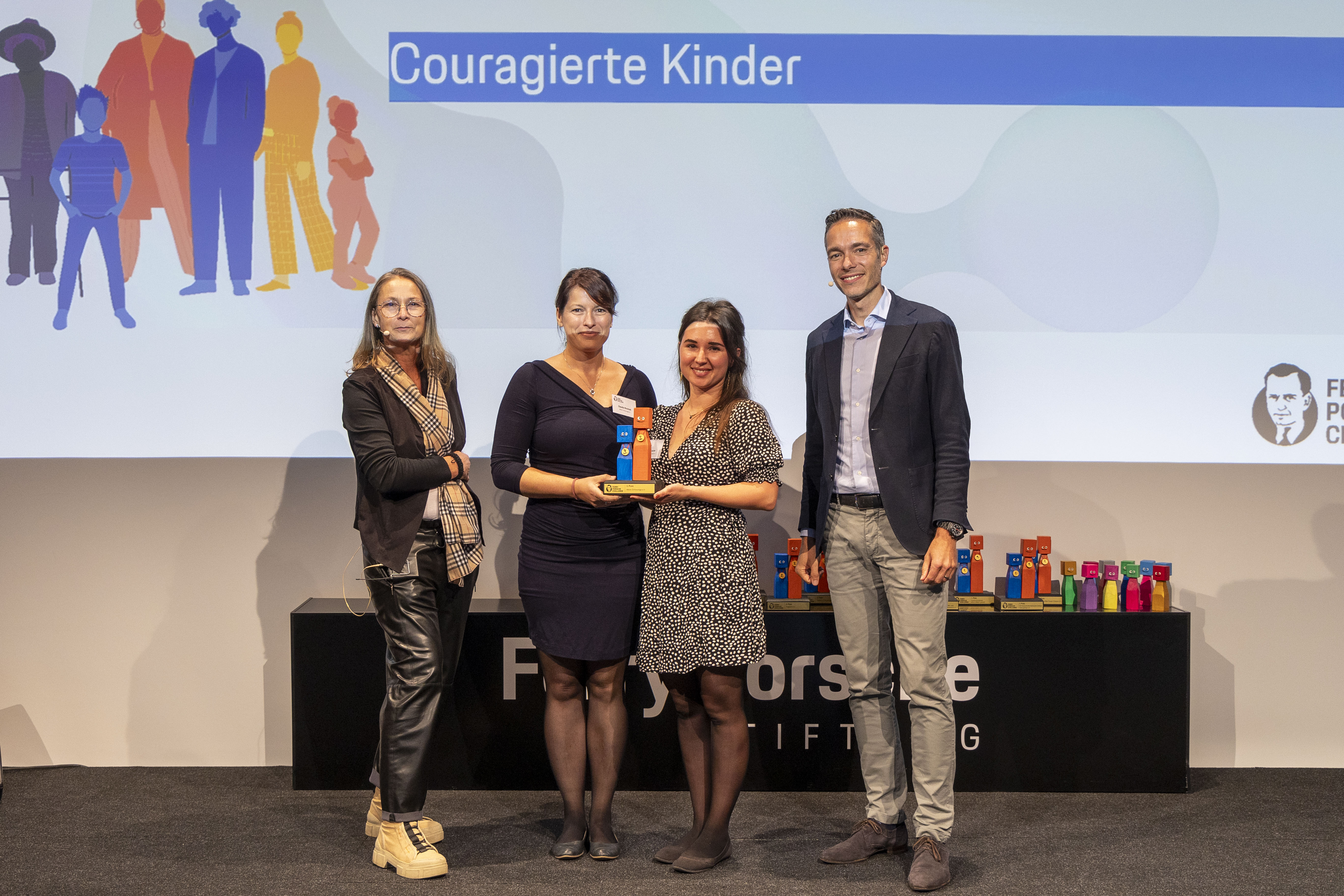 KI generiert: Das Bild zeigt eine Gruppe von vier Personen auf einer Bühne, die eine Auszeichnung oder einen Preis erhalten. Im Hintergrund ist eine Präsentation mit dem Titel "Couragierte Kinder" und dem Logo der "Frankfurter Buchmesse" zu sehen.