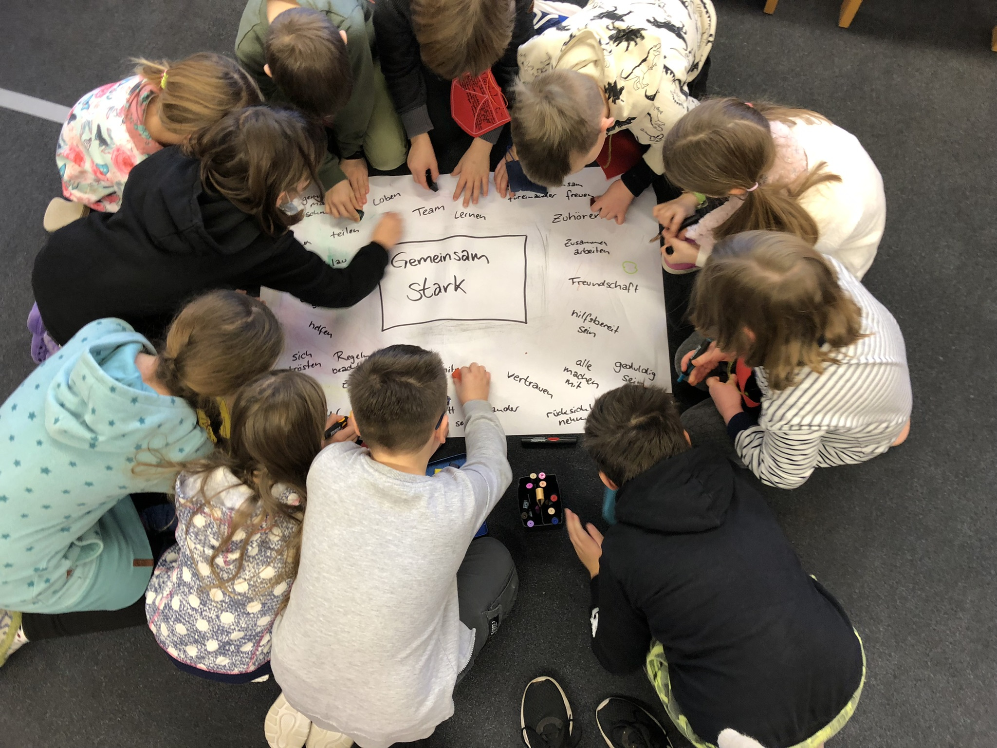 KI generiert: Das Bild zeigt eine Gruppe von Kindern, die sich um ein großes Blatt Papier versammelt haben und gemeinsam Ideen sammeln oder eine Aufgabe bearbeiten. Der Hauptinhalt des Bildes ist die Zusammenarbeit und Interaktion der Kinder bei einer Gruppenaktivität.