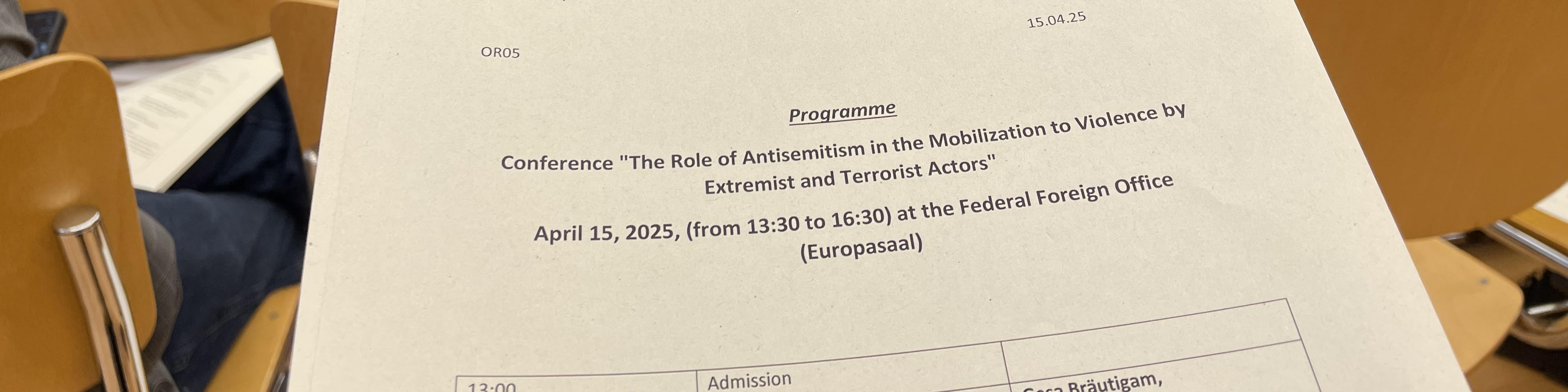 KI generiert: Das Bild zeigt ein Programm für eine Konferenz mit dem Titel "The Role of Antisemitism in the Mobilization to Violence by Extremist and Terrorist Actors", die am 15. April 2025 von 13:30 bis 16:30 im Bundeshaus (Europasaal) stattfindet. Der Hauptinhalt des Bildes ist die Ankündigung dieser Konferenz und deren Details.